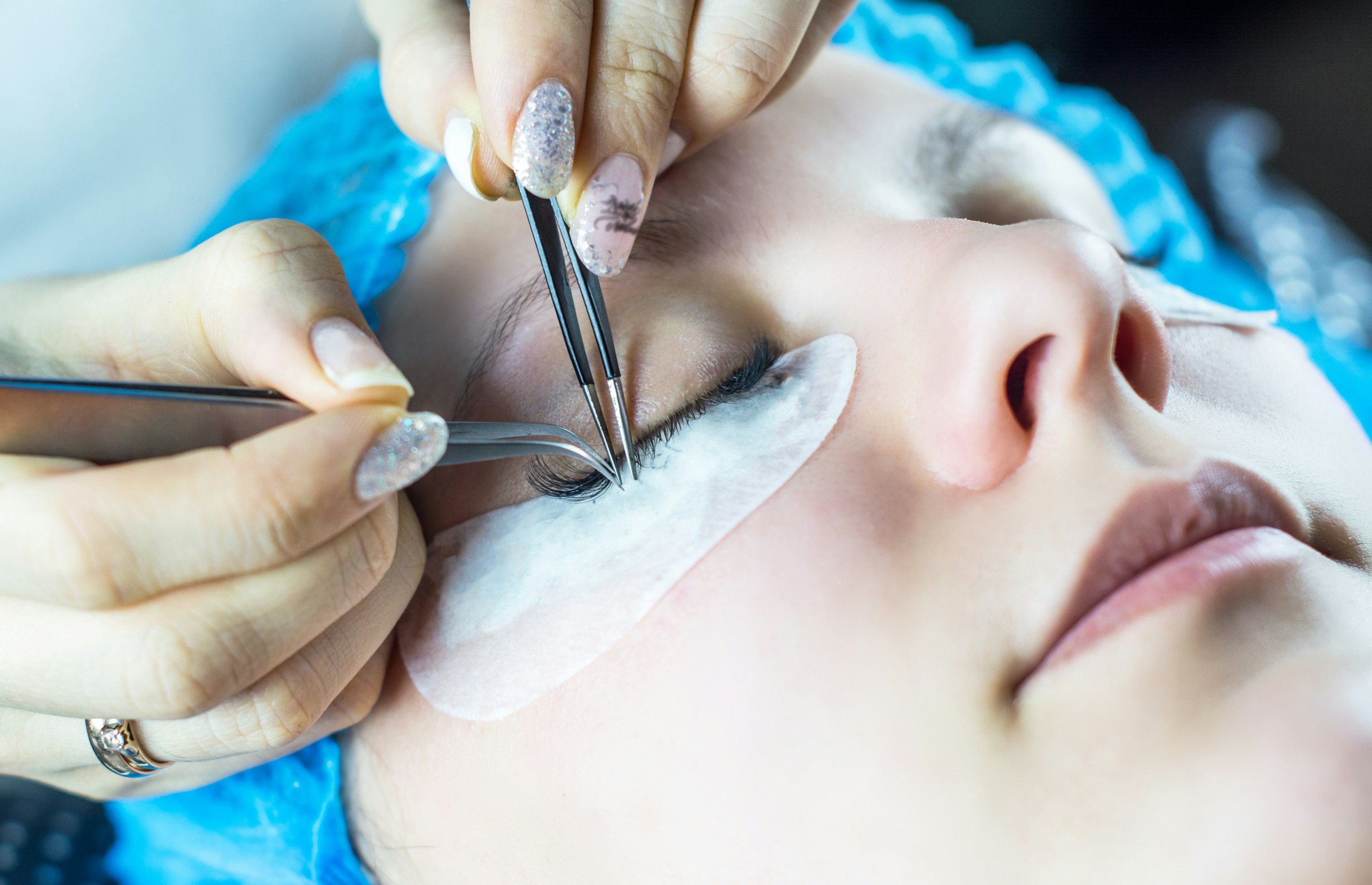 High fidelity hands-only placeholder of lash extensions being applied with tweezers and a white under-eye pad